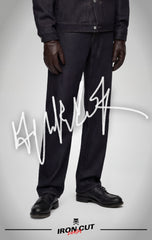 A person wearing IRON CUT black straight-leg jeans with black leather shoes and a matching denim jacket.