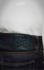 Embossed skull and crossbones leather patch on the waistband of indigo denim.