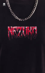 Close-up of the front of a black t-shirt featuring a "Nezuko" logo in a red and white dripping, heavy metal-style font, styled with a silver cuban link chain.