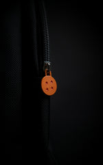 Macro shot of a custom orange circular zipper pull designed to look like the iconic 4-star Dragon Ball with red star engravings on a black zipper track.