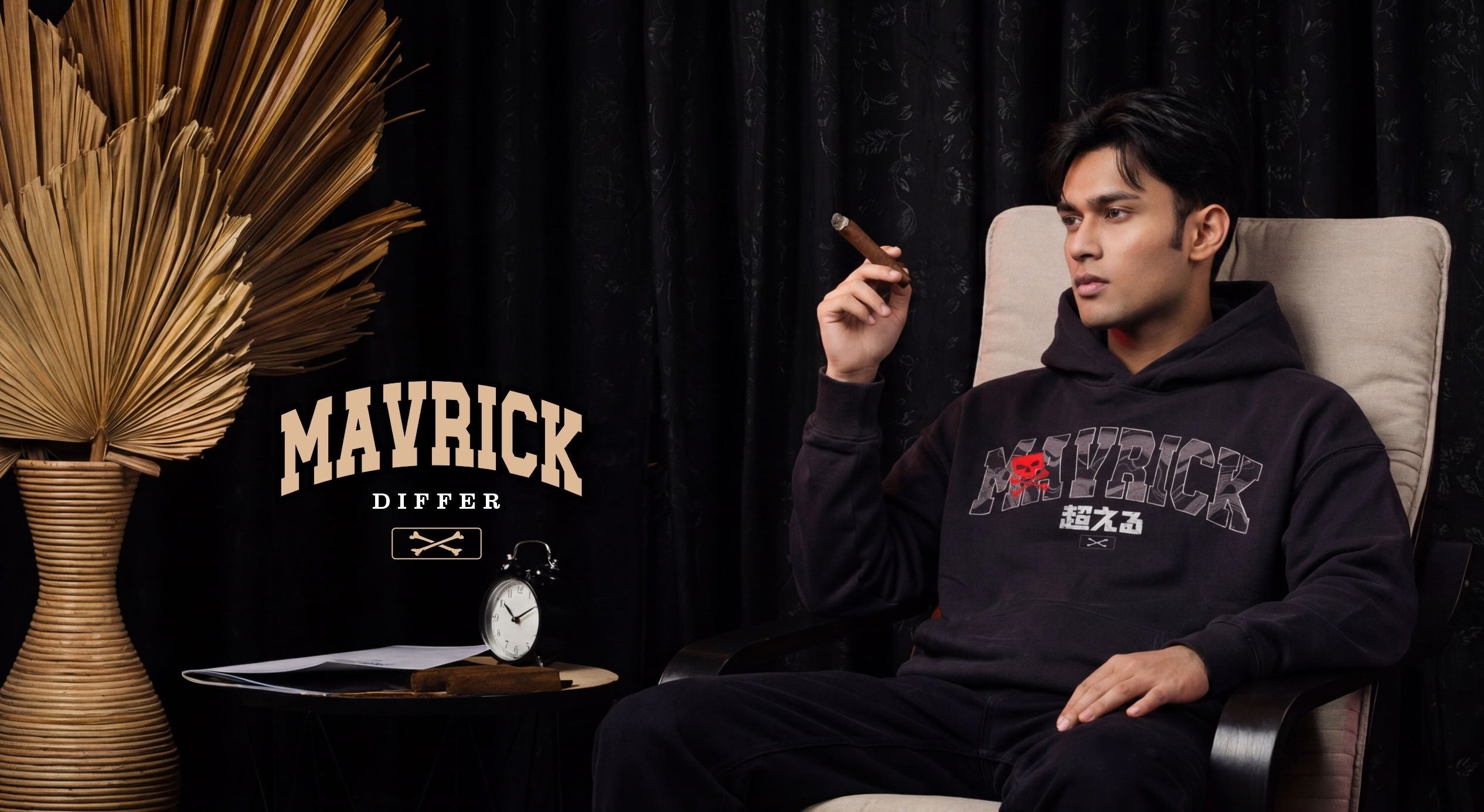 Man wearing a black hoodie with 'MAVRICK' branding, sitting in a chair against a dark curtain background.1621243260e1af0c20-0