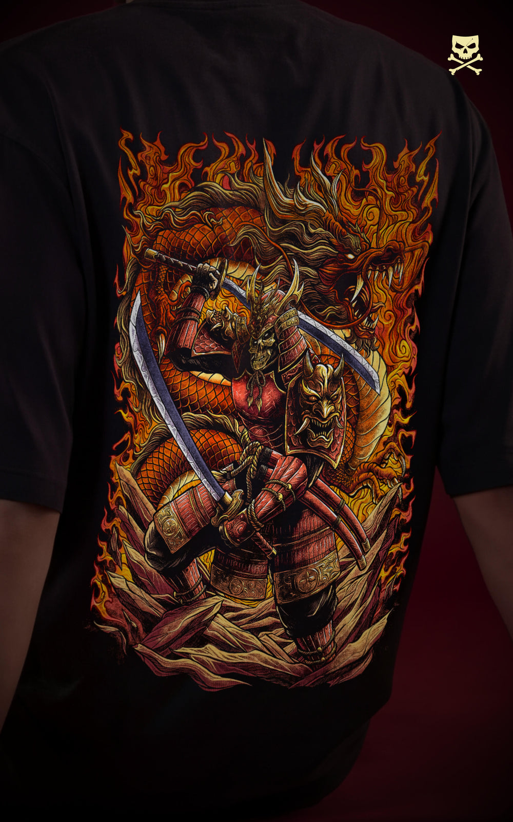 
Close-up of the back of a black t-shirt featuring a detailed graphic of a skeletal samurai warrior wielding dual katanas. The character is framed by a coiled orange dragon and intense orange flames in a traditional Japanese art style.