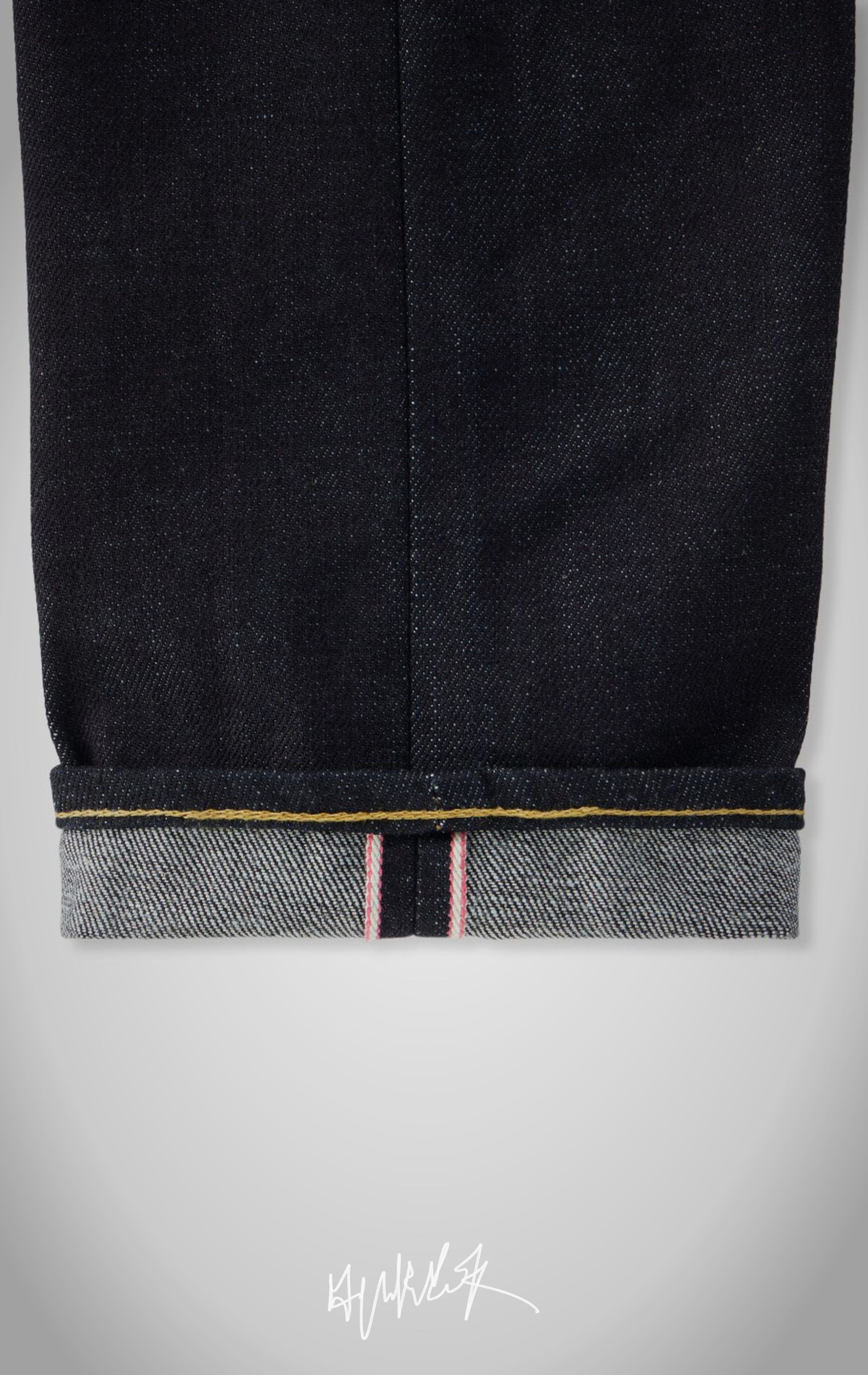 Close-up of the red and white selvedge ID on a cuffed indigo denim hem.