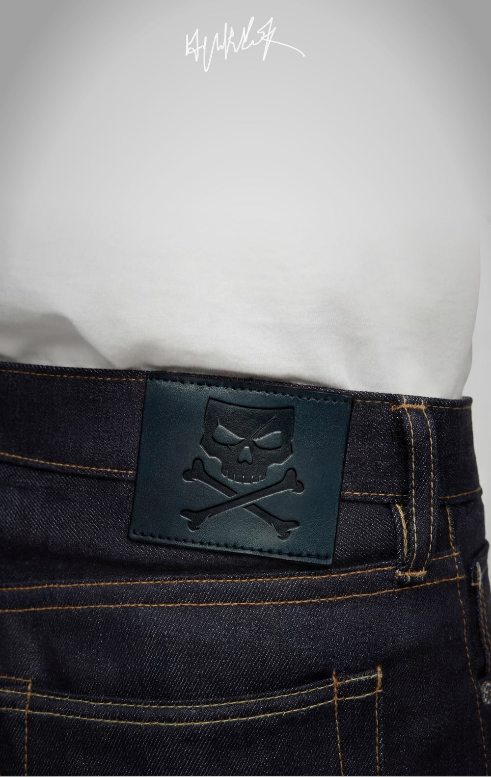 Embossed skull and crossbones leather patch on the waistband of indigo denim.