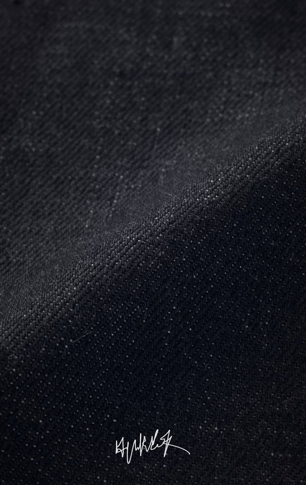 Close-up macro shot showing the texture of dark indigo raw selvedge denim.