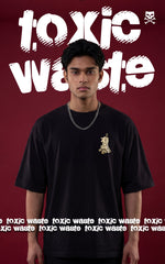 Front view of a male model wearing an oversized black streetwear t-shirt featuring a small chest graphic and a silver chain necklace. The background shows "Toxic Waste" typography in a distressed white font against a dark maroon backdrop.
 
