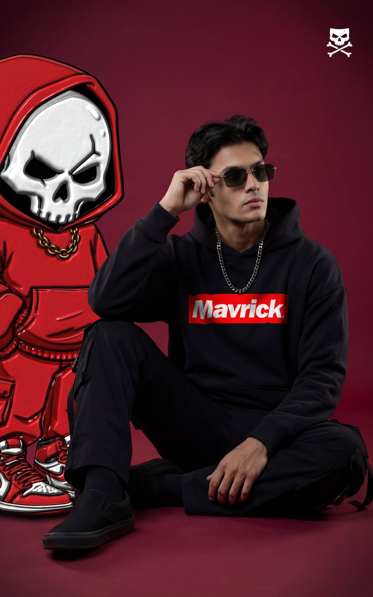 Full-body shot of a man in a black Mavrick box logo hoodie and black cargo pants, sitting in a stylish urban streetwear pose against a maroon background.