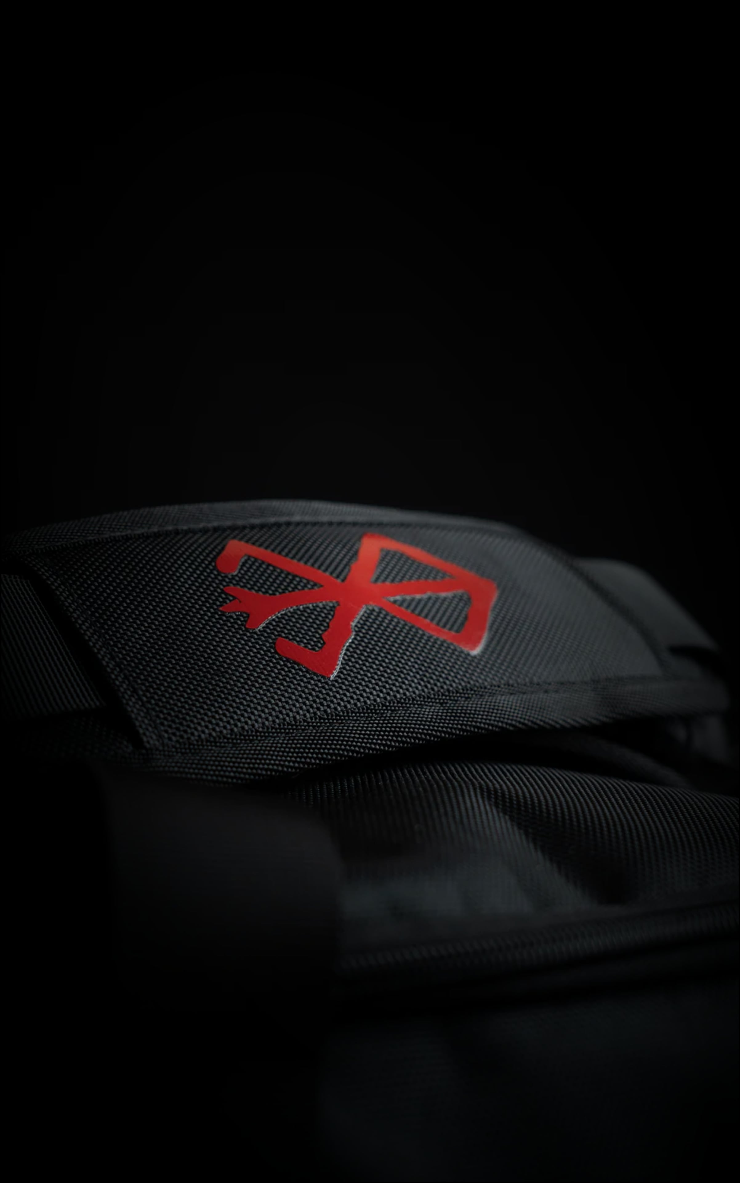 Close-up of the padded handle wrap on the Guts duffle bag featuring a vibrant red embroidered Brand of Sacrifice logo on black heavy-duty canvas.