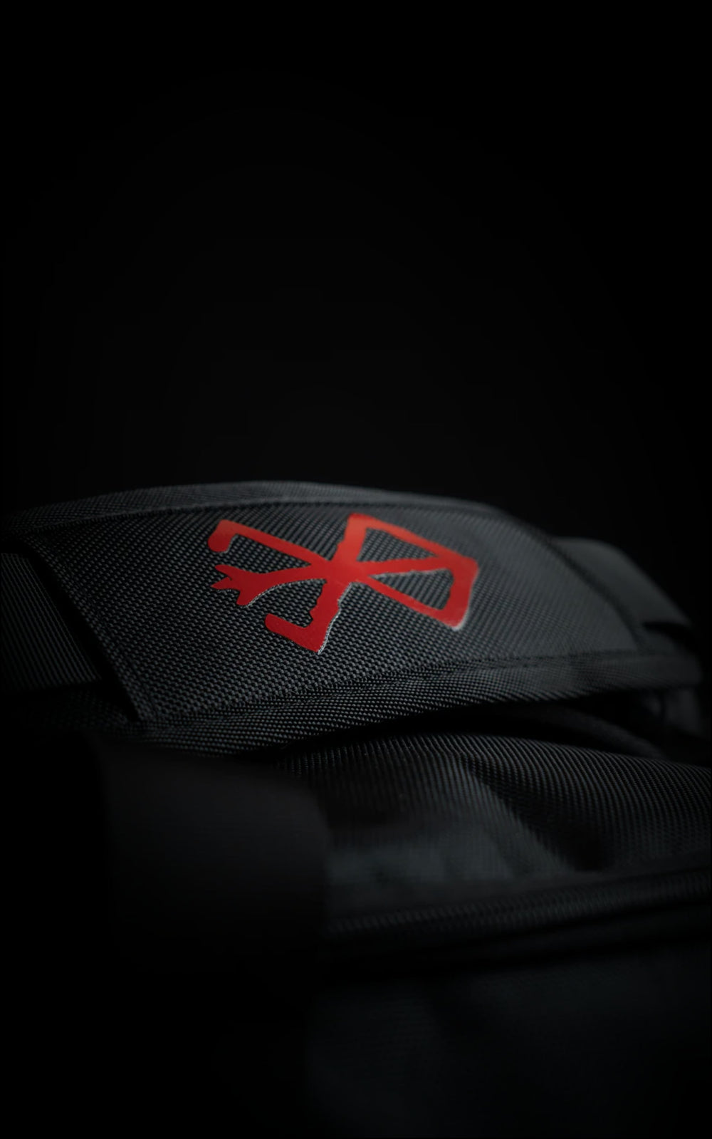 Close-up of the padded handle wrap on the Guts duffle bag featuring a vibrant red embroidered Brand of Sacrifice logo on black heavy-duty canvas.