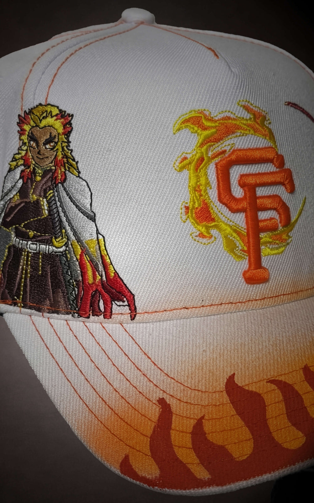 Close-up of flaming logo embroidery and Rengoku character detail on a white 5-panel snapback.
