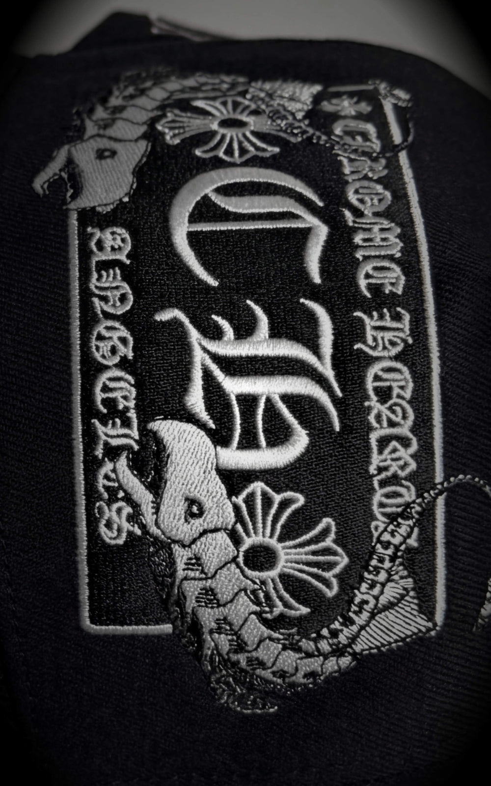 Detailed close-up of a high-stitch count anime character embroidery (Chrollo Lucilfer) on the side panel of a black streetwear hat.