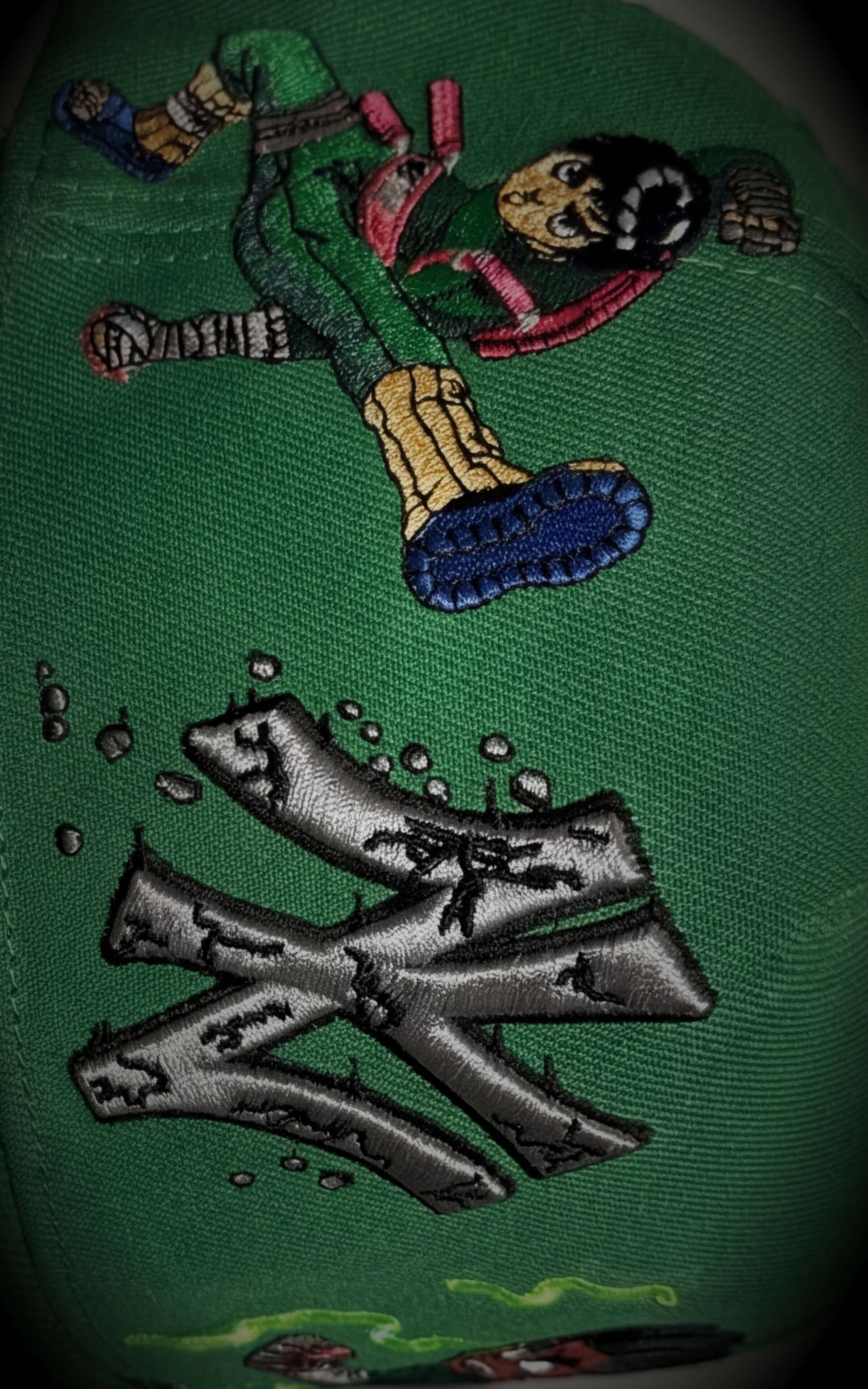 Detailed close-up of a stylized "NY" logo with stone-crack texture and Rock Lee character embroidery on green fabric.	