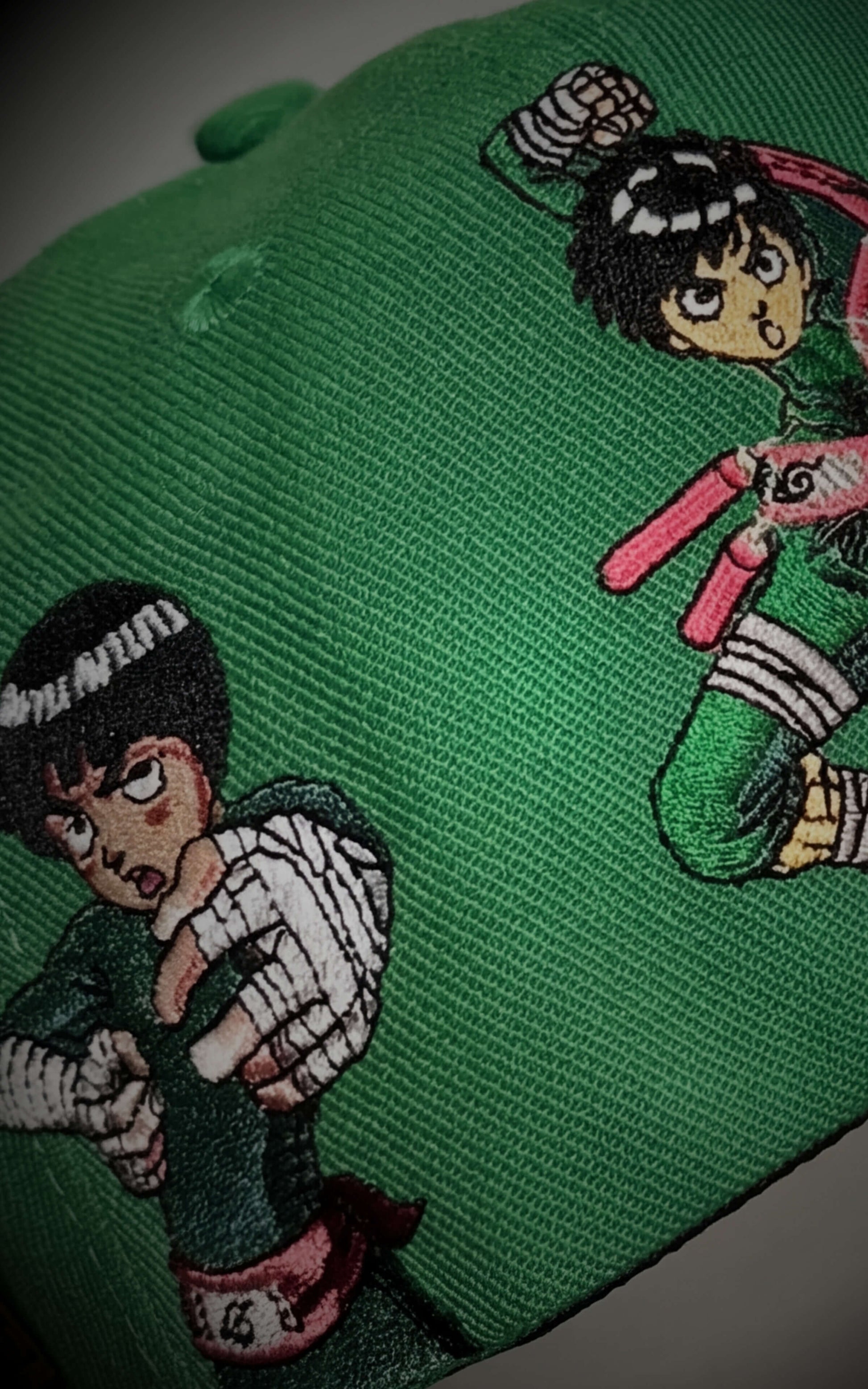 Macro shot of multiple Rock Lee character poses embroidered on a premium green 5-panel snapback.

