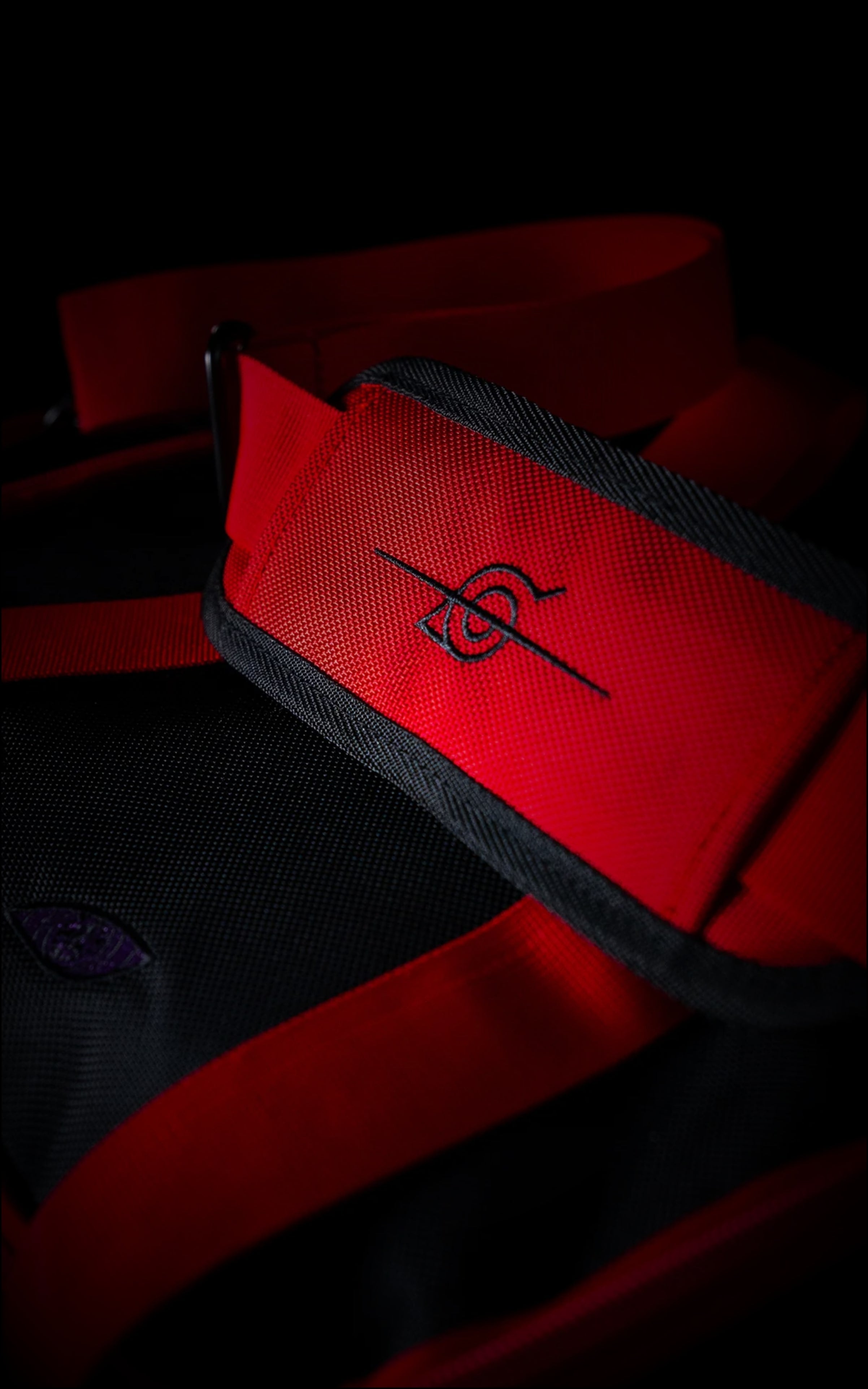Close-up of the red padded shoulder strap on the Rogue Ninja duffle bag featuring a black embroidered "crossed-out" Hidden Leaf Village (Konoha) symbol.
