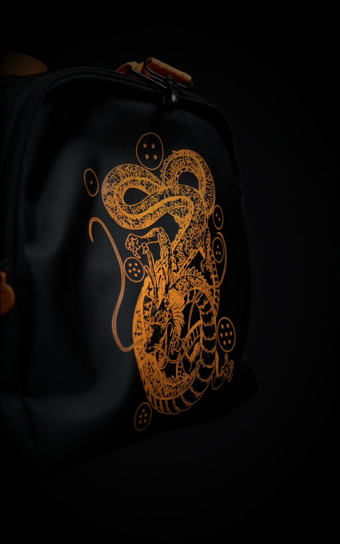 Full view of the black and orange Saiyan Duffle Bag featuring a large embroidered Goku "Go" Kanji symbol on the front pocket and vibrant orange straps.