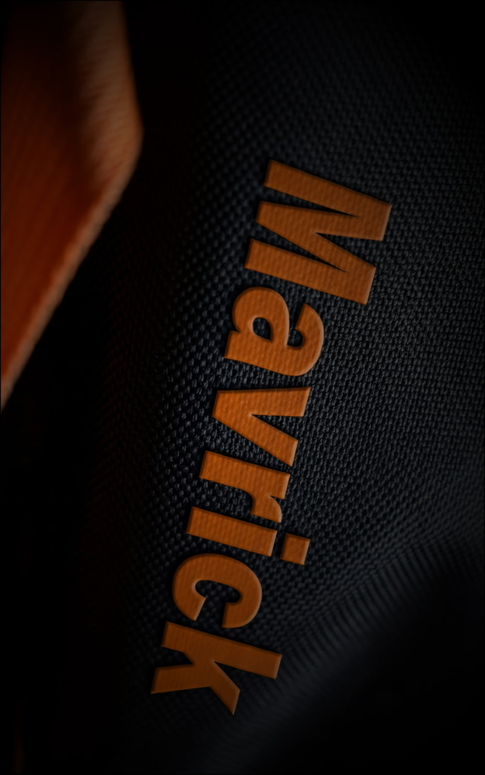 Close-up of the orange raised 3D "Maverick" logo text on the heavy-duty black canvas material of the Saiyan anime travel bag.