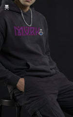 Front view portrait of a man wearing a MVRK streetwear hoodie with a flaming logo and Sukuna’s facial curse markings on the chest, paired with a silver chain and sunglasses.